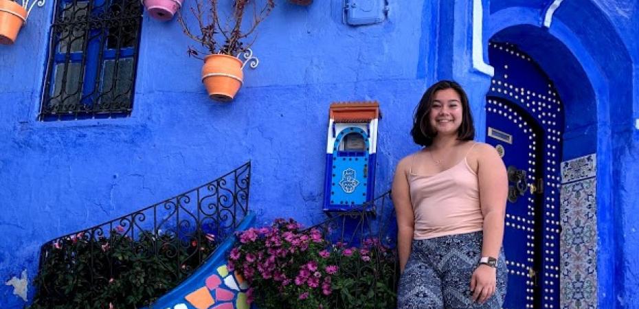 A student stands against a blue building during her study abroad