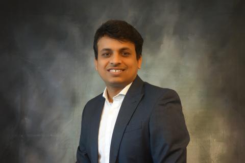 Vivek sits facing the camera, smiling, in front of a gray background