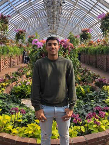 Sharan stands facing the camera inside a greenhouse filled with flowers