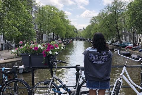 A student with a CWRU shirt on looks at a river between two rows of buildings and trees