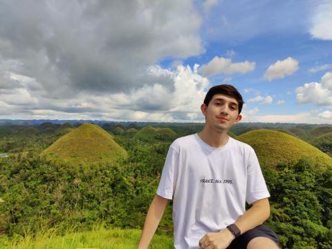 David sits in front of mountains in Southeast Asia while on his study abroad
