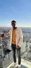 Ibrahima stands on a balcony with a city view behind him while on study abroad