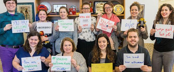 Staff holding up signs that say You Are Welcome Here in multiple languages
