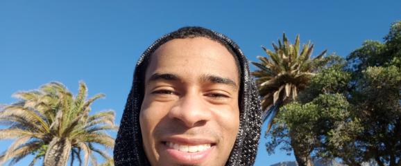 Carlos Lewis-Miller standing outside with his hood on in front of palm trees