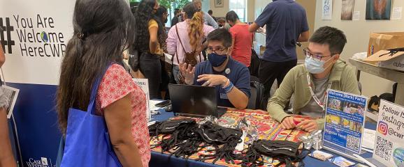 An international student advisor and ISAC representative speak with someone at the Student Information Fair while wearing masks