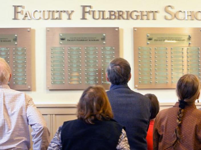 Faculty members looking at the plaques of the Fulbright winners on the wall on campus