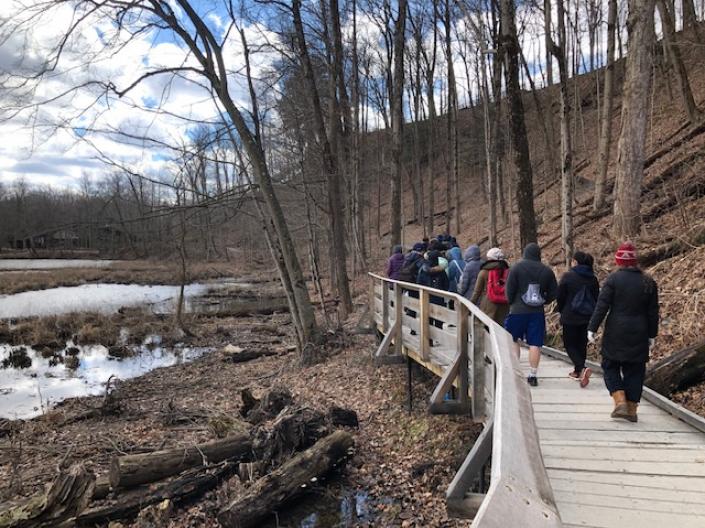 CWRU students hike through trees over a wooden bridge in the Cleveland Metroparks
