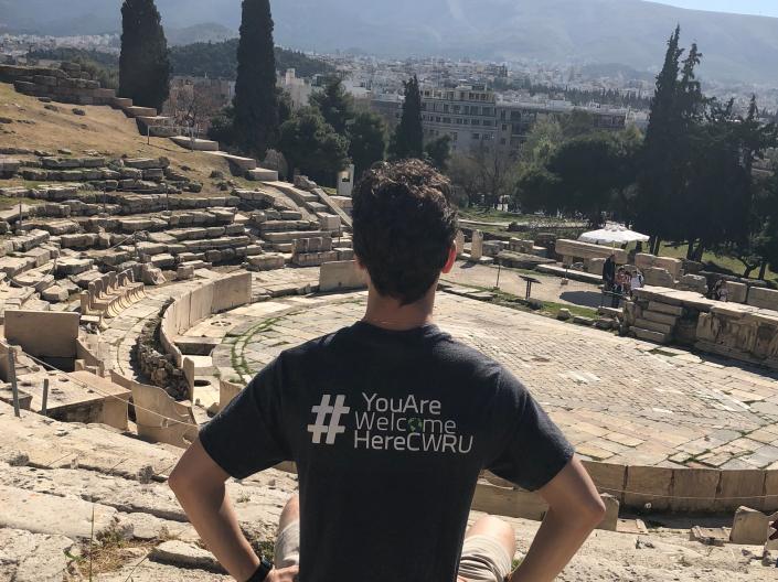Michel Yuzik sitting outside with a #YouAreWelcomeHereCWRU tee shirt on