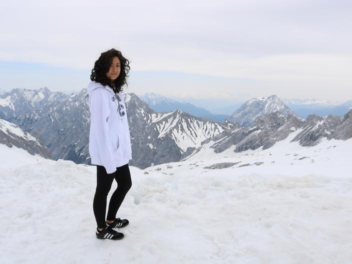 A student stands in the snow overlooking a snowy mountain