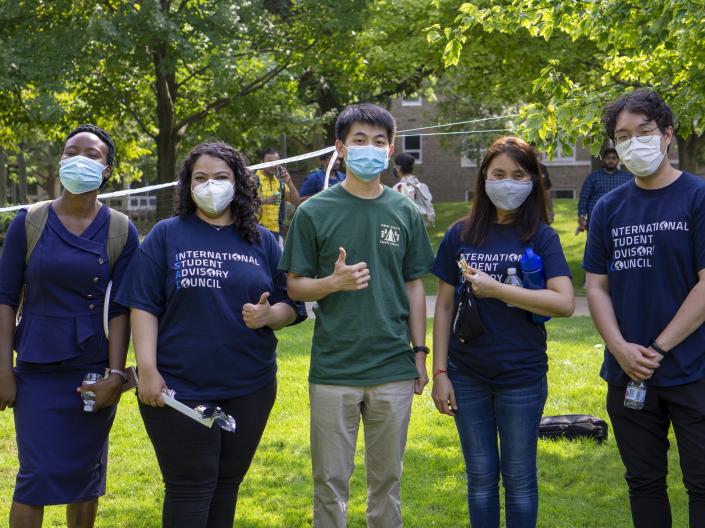 A group of international students stand together outside for a picture, some wearing shirts that read "International Student Advisory Council"