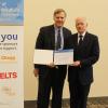 Two men standing next to banner pose holding certificate