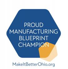 Bluepring badge is a large blue hexagon with the words "Proud Manufacturing Blueprint Champion" with a smaller yellow hexagon merging into its space