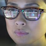Image of a computer screen reflected in a closeup of a women's face wearing glasses
