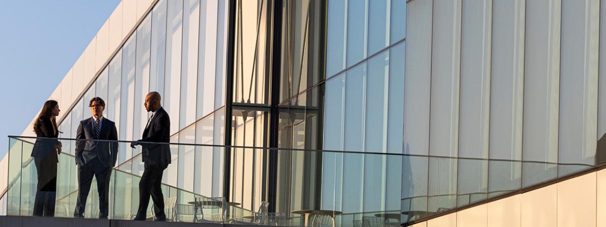 Law students standing on the outdoor terrace of a modern glass campus building.