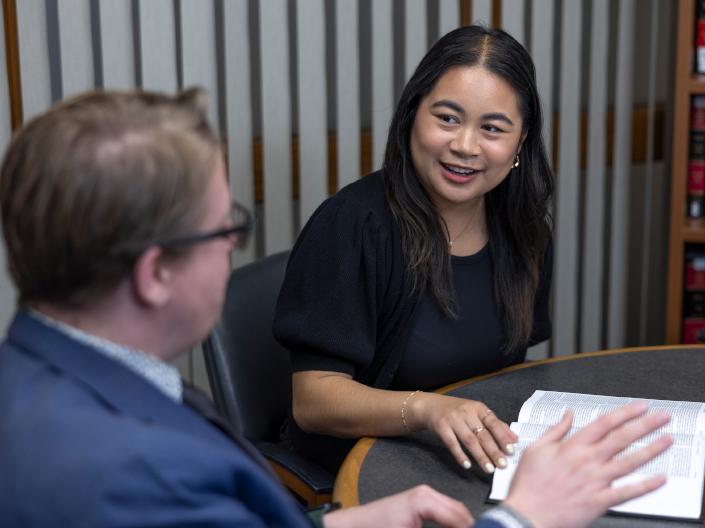 A smiling woman in a black top talks with a man in a blue suit at a table with an open book.
