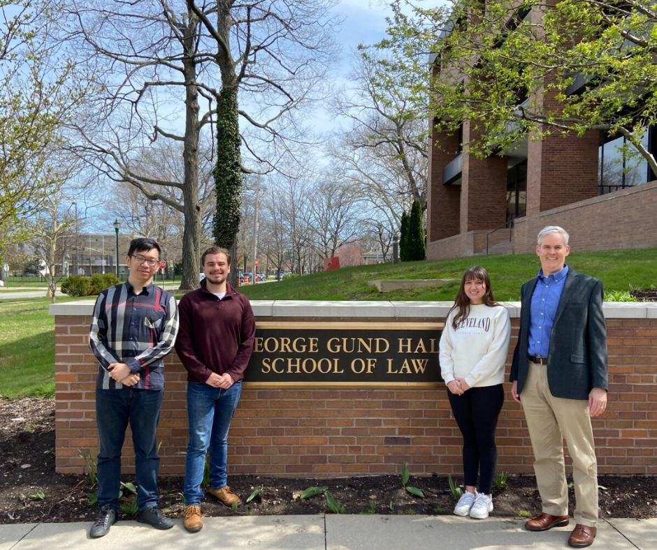 Three students and their professor in front of Gund Hall Case Western Reserve School of Law sign