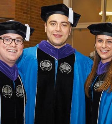 Three PhD graduates stand for a photo