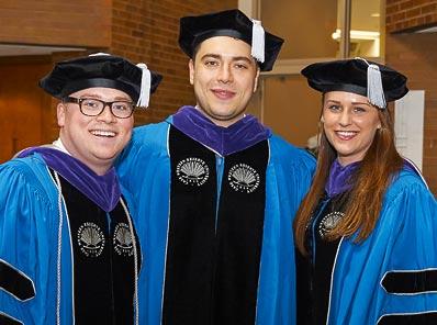 Three PhD graduates stand for a photo