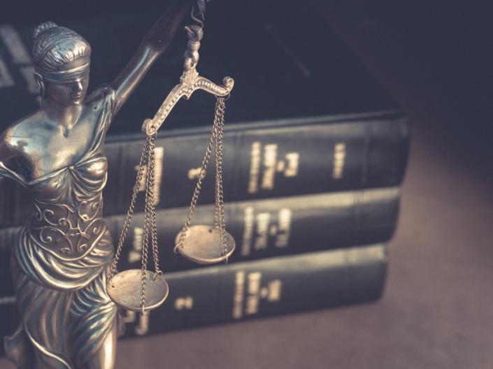 A figure of Lady Justice positioned in front of three law books.