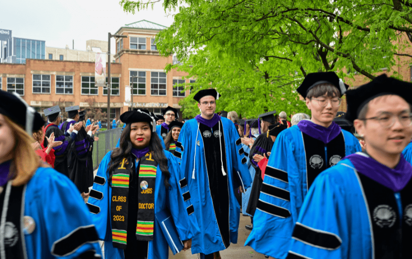 Students walking towards the camera, dressed in commencement regalia
