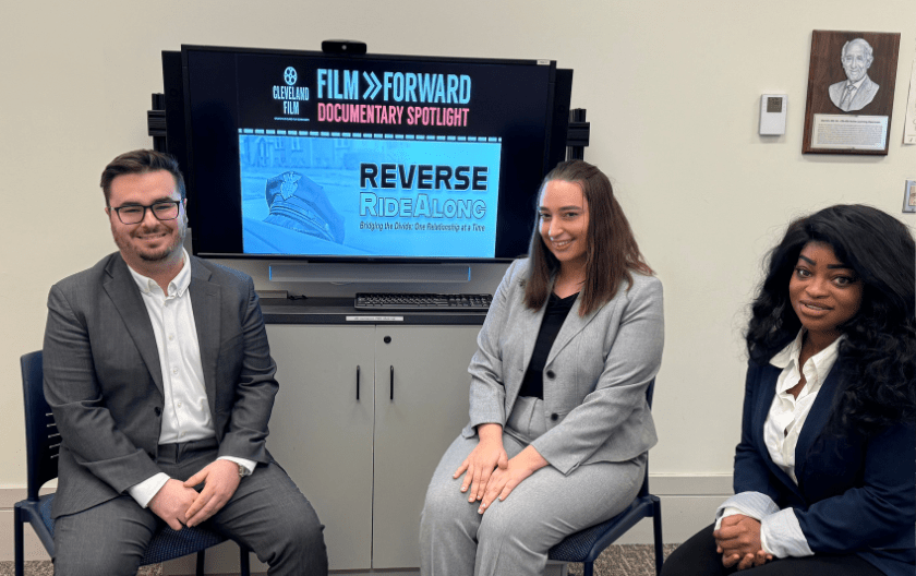 From left to right: Joel Shambaugh, Kayla DePalma and Maria Kargbo sitting in front of a flyer for the Reverse RideAlong film 