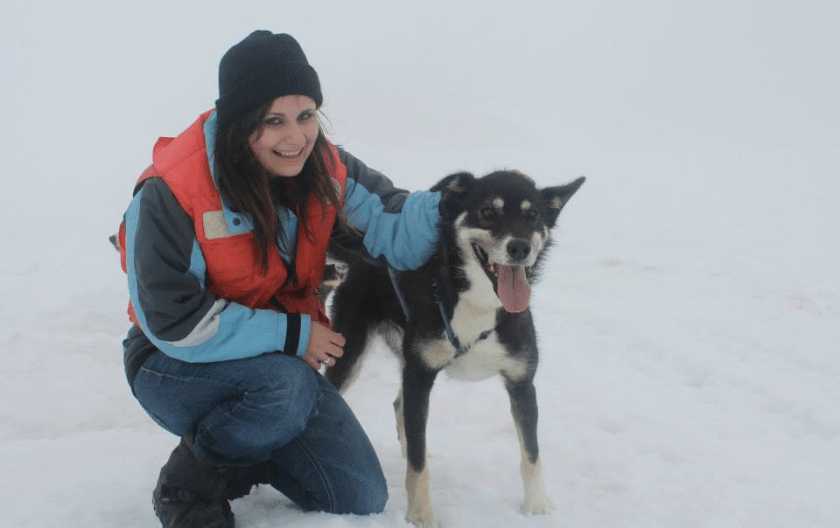 Tiffany Johnston in the snow, crouched next to a dog