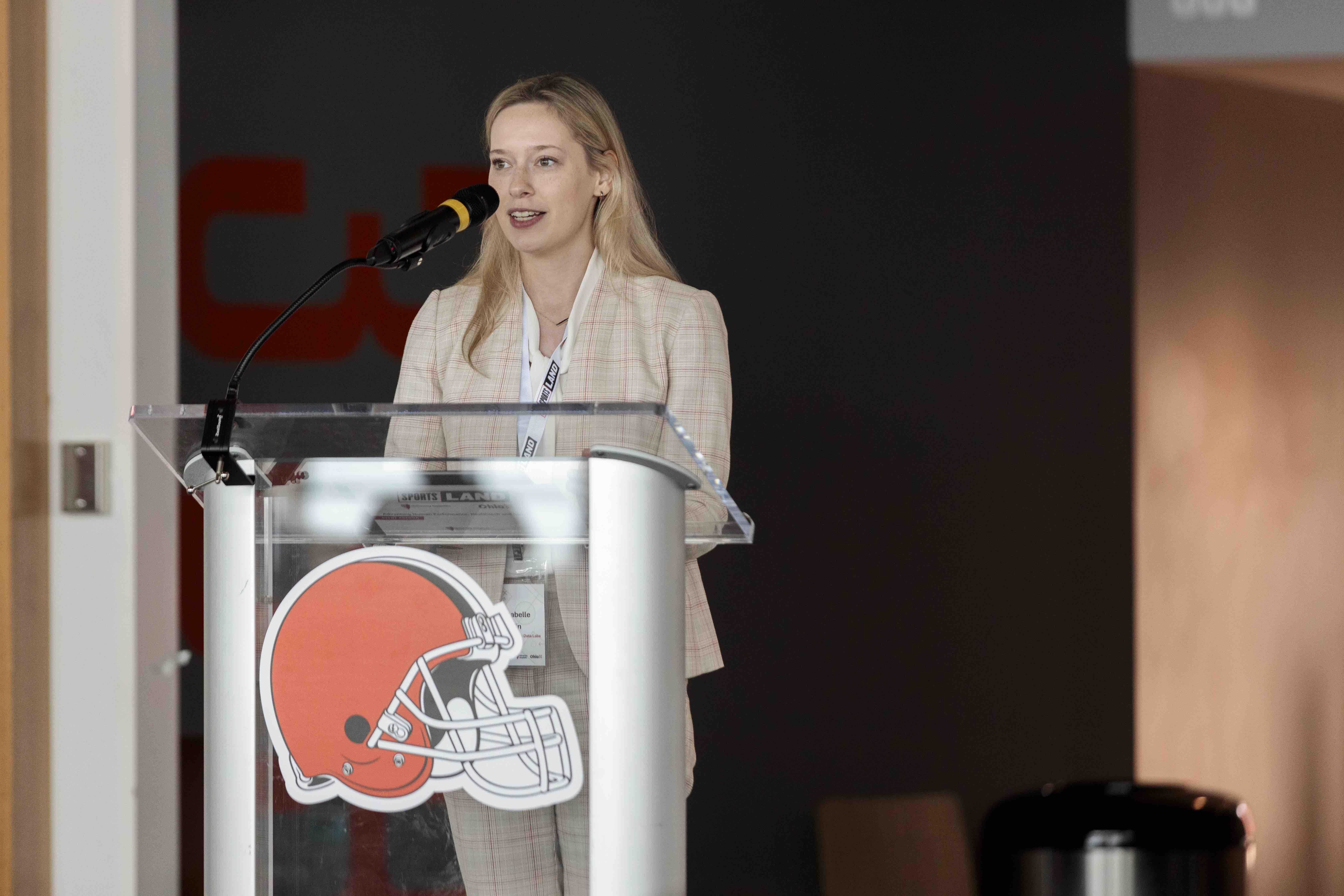 Annabelle Lincoln presenting at SportsLand Summit behind a podium with a Cleveland Browns logo on it