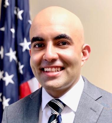 Sanjeev Bhasker headshot in front of an American flag. 
