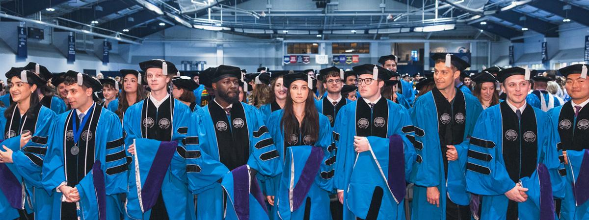  A group of diverse law school graduates in full academic regalia (blue robes and black mortarboards) standing together after a commencement ceremony.
