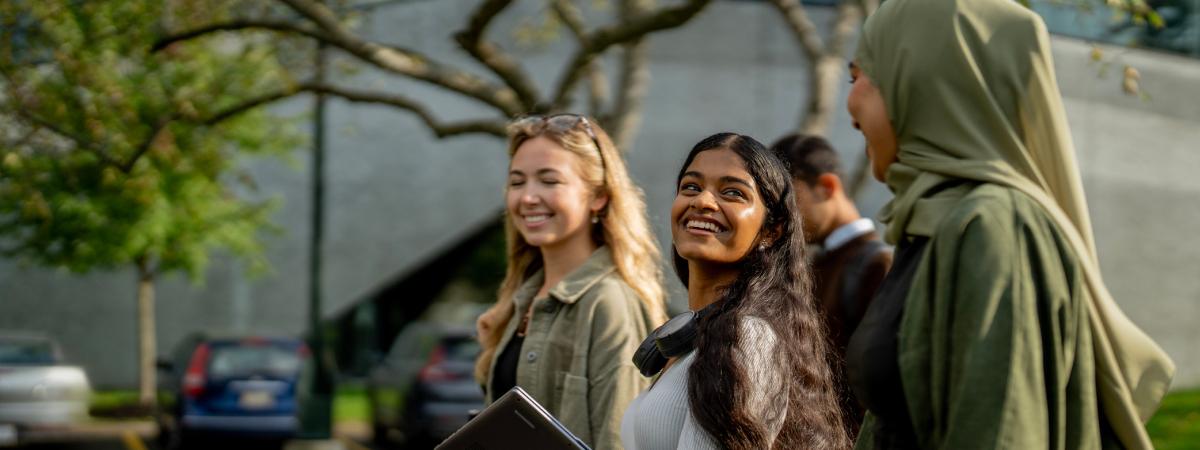 A diverse group of female students smiling and walking outdoors on campus.