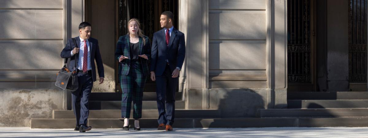 Three students in business attire walk down the steps of a building together.
