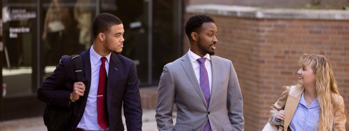 Three students in business attire talk and walk together.