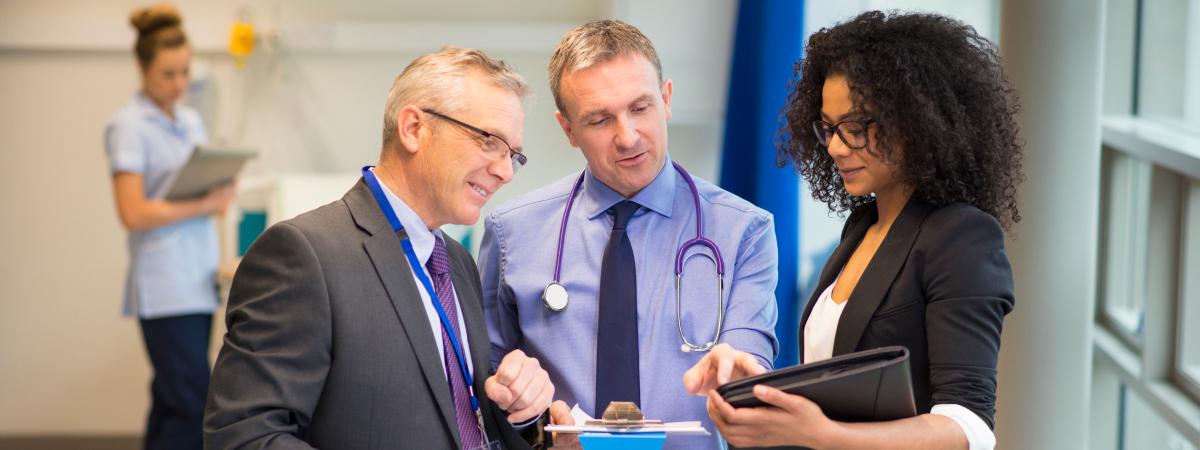 A doctor and two professionals reviewing a tablet in a hospital hallway.
