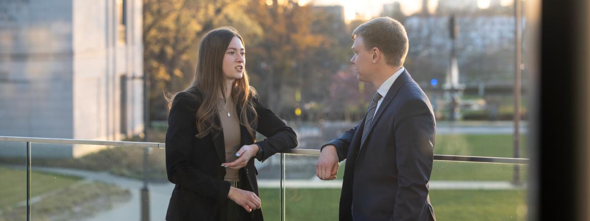 Two professionals conversing on an outdoor campus terrace.
