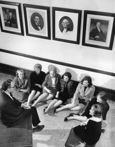 Group of female lawyers sitting on the floor listening to a male speaker