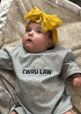 Baby Evie pictured in a "CWRU Law" onesie, wearing a yellow bow on her head