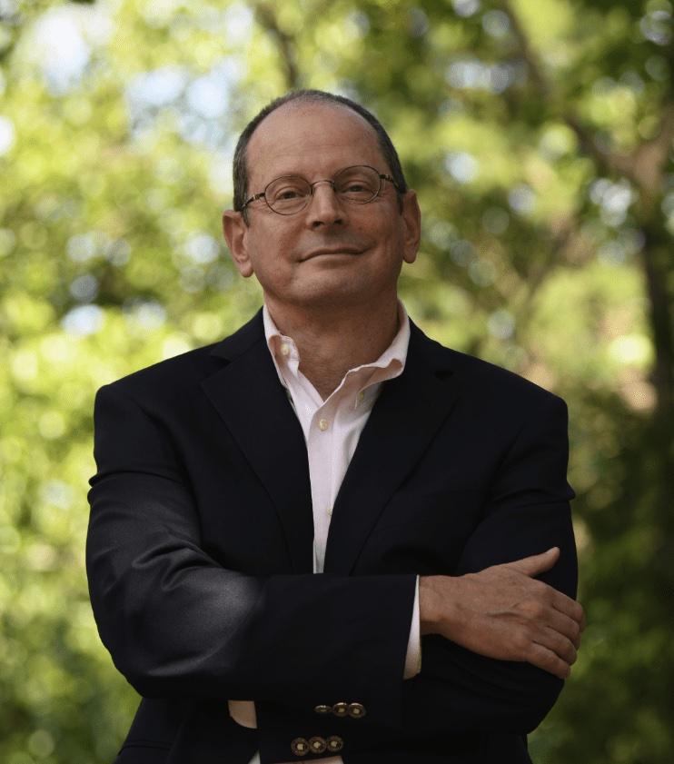 Jonathan Rauch semi-professional headshot, standing with a background of greenery and his arms crossed