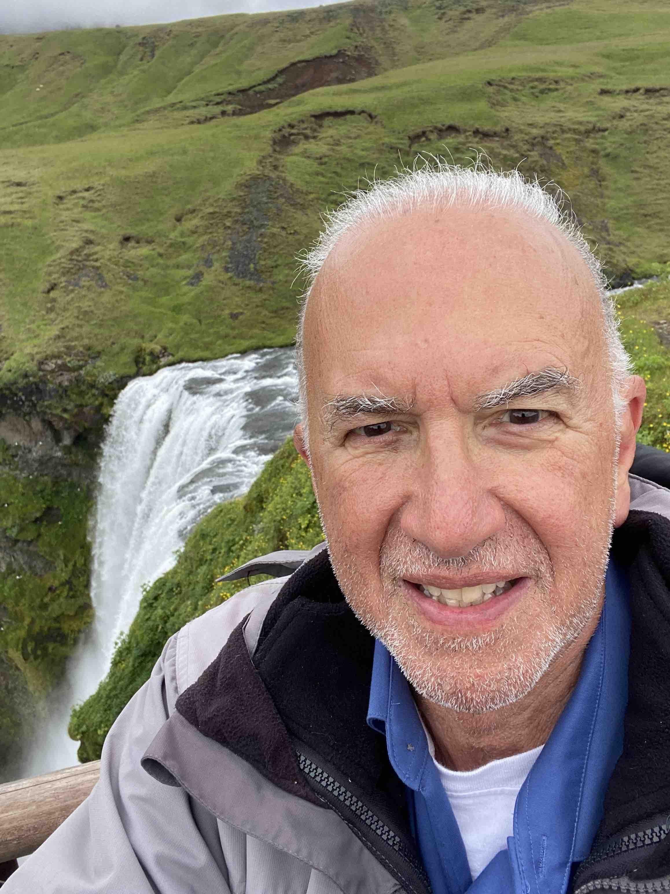 A selfie of Dr. Stuart Bussey, taken in front of green fields and a waterfall