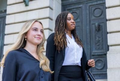 Two women in business attire walk on the steps of a building.
