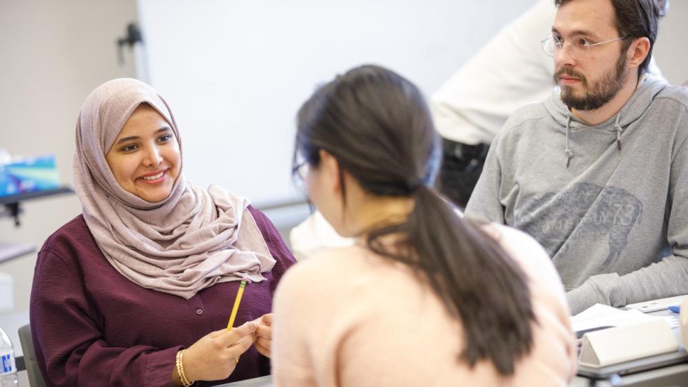 Three students work together in class while smiling.