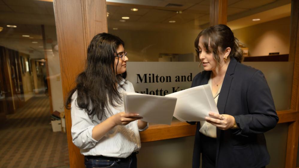 Two students in business attire talk together in front of the Kramer Law Clinic.
