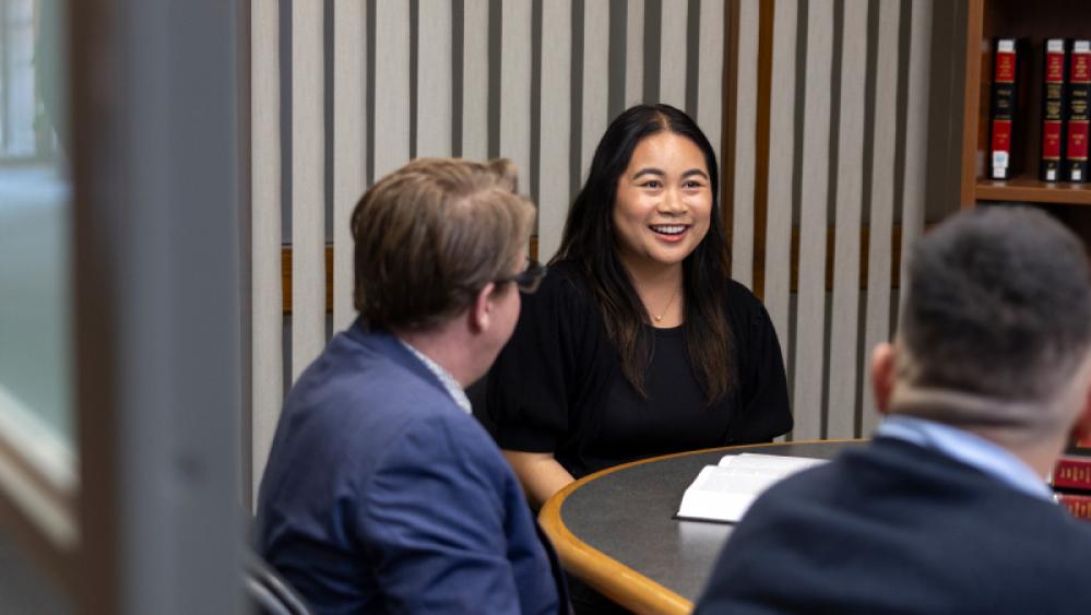 A group of students sitting around a table with stacks of law books in a library study room.