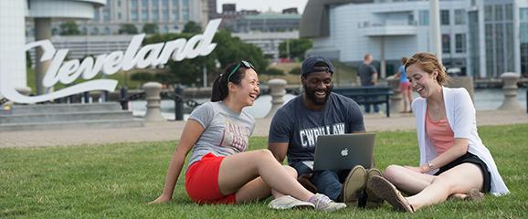 three case western reserve university students sitting on the grass in front of the rock and roll hall of fame in downtown cleveland