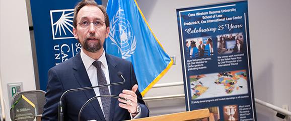 speaker giving a presentation behind a lecturn, with a case western reserve university banner in front and back wall, and united nations flag in background