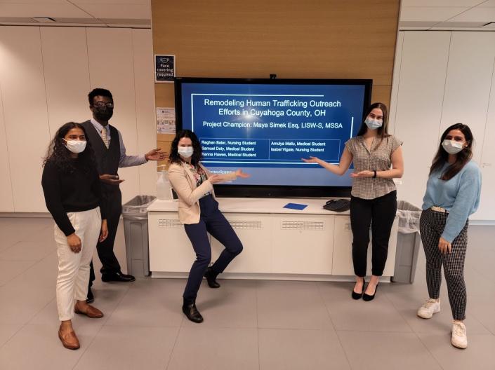A diverse group of individuals wearing face masks standing in front of a large screen.