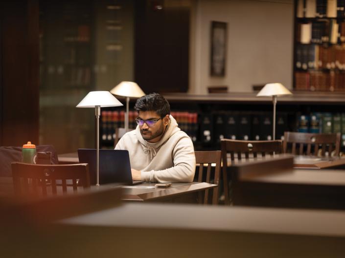 A student works on his laptop, alone in the Law library.