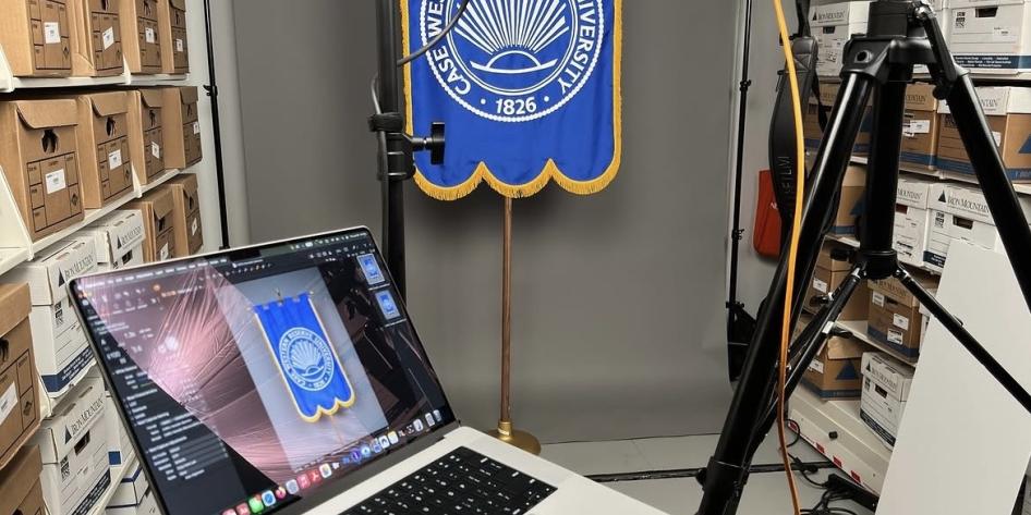CWRU heraldic banner hangs in front of camera and computer for digitization.