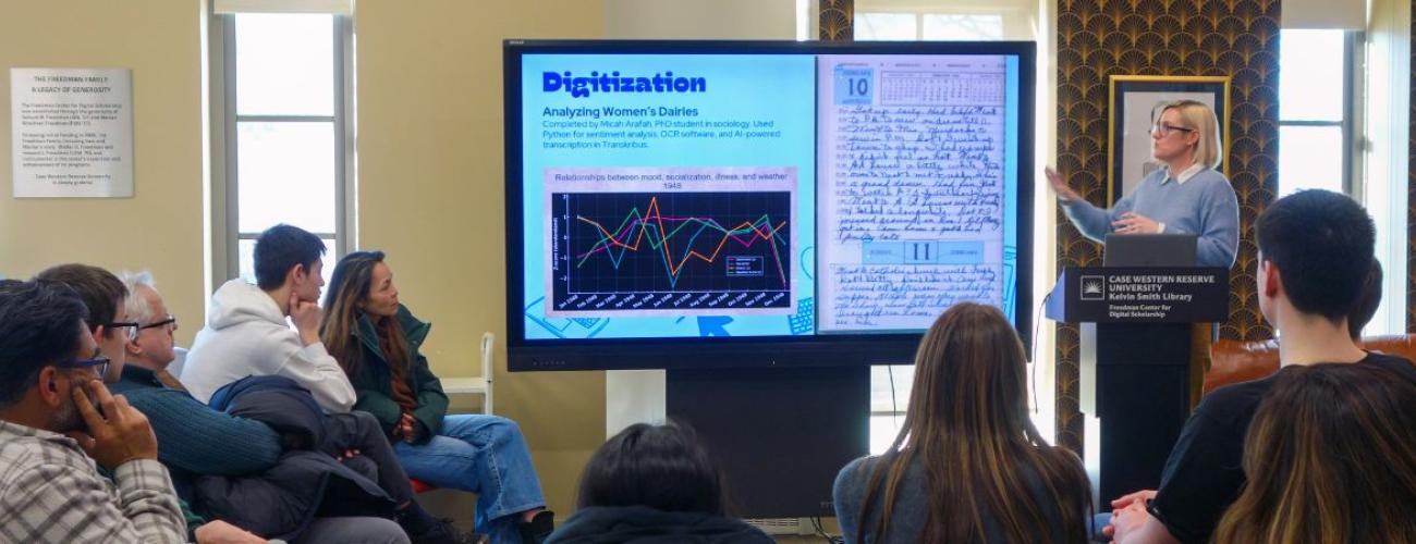 People listen and watch a speaker present information on a screen. 