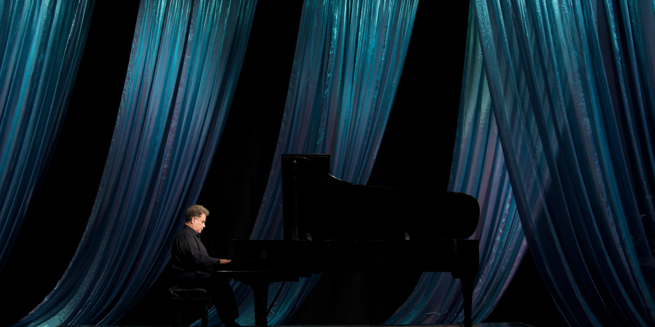 Jeffrey Siegel playing piano with a curtain behind him