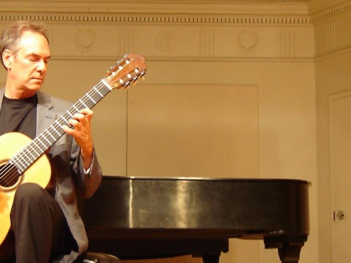Guy holding a guitar and sitting in a chair